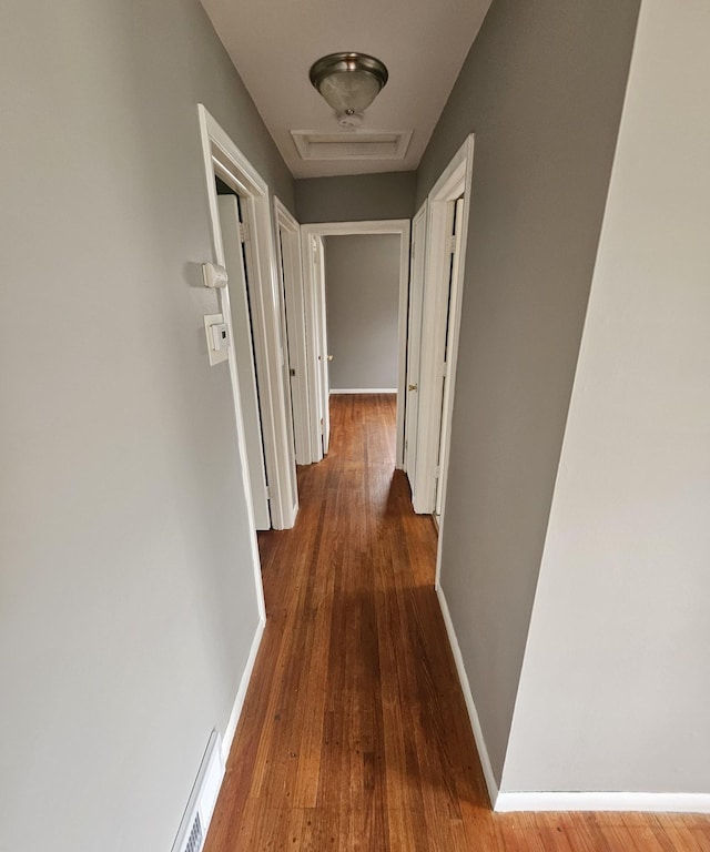 hallway with baseboards, wood finished floors, and visible vents