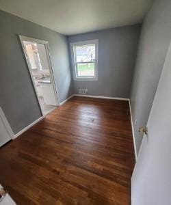 unfurnished bedroom with connected bathroom, baseboards, and wood finished floors