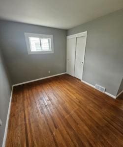 unfurnished bedroom featuring visible vents, baseboards, wood finished floors, and a closet