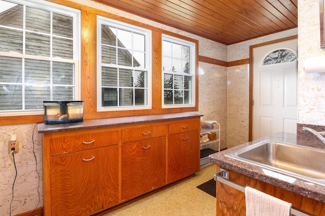 kitchen with dark countertops, brown cabinetry, a sink, and wallpapered walls