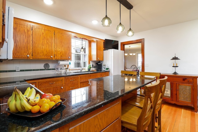 kitchen with a sink, a breakfast bar area, brown cabinets, and a notable chandelier
