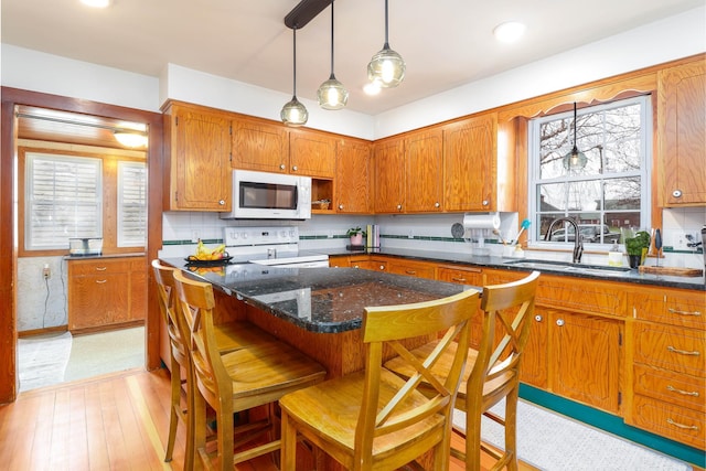 kitchen with a sink, brown cabinetry, white appliances, and a healthy amount of sunlight