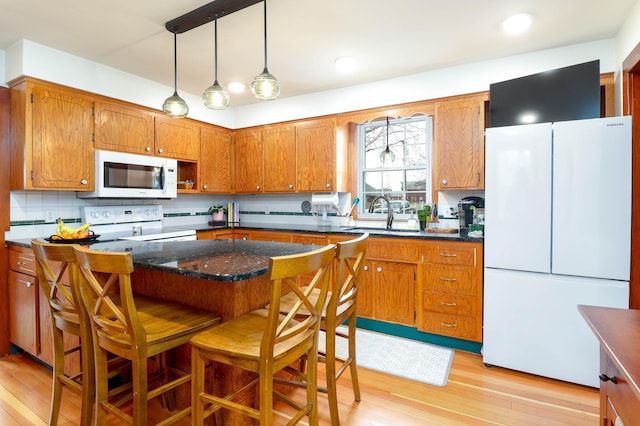 kitchen featuring a sink, light wood finished floors, brown cabinets, and white appliances