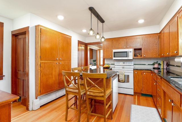 kitchen featuring backsplash, baseboard heating, brown cabinets, light wood finished floors, and white appliances