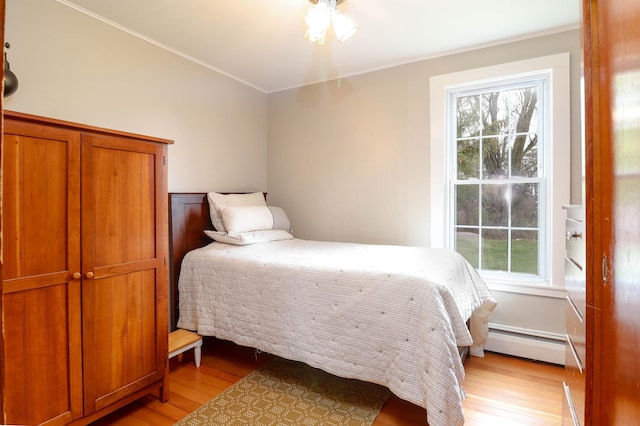 bedroom featuring a baseboard heating unit, multiple windows, ornamental molding, and light wood-type flooring