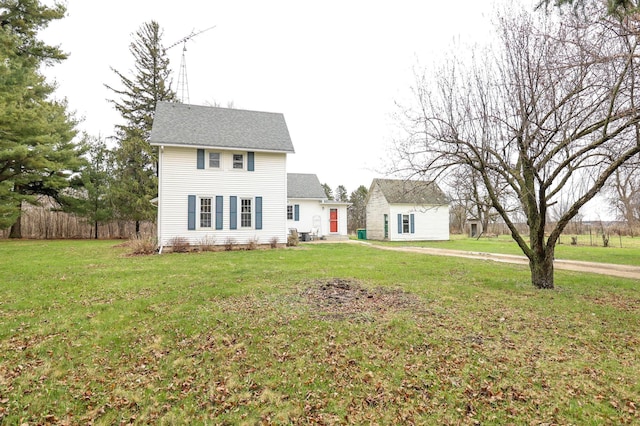 colonial-style house featuring fence, an outbuilding, roof with shingles, and a front lawn