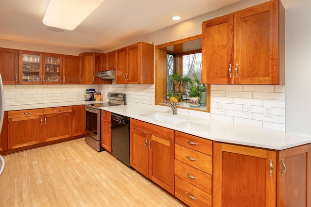 kitchen featuring stainless steel electric range, a sink, brown cabinetry, black dishwasher, and under cabinet range hood