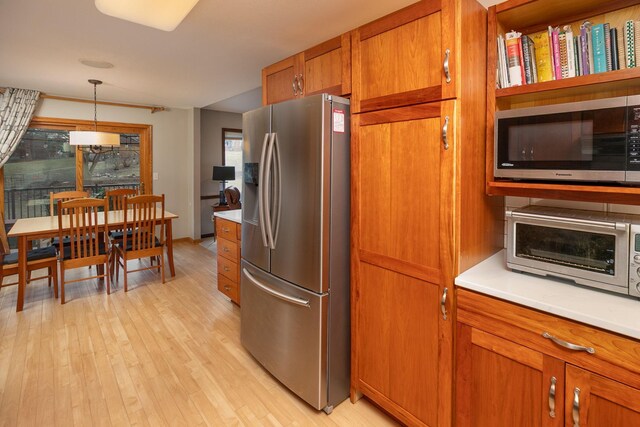 kitchen with pendant lighting, light wood-style floors, light countertops, brown cabinets, and appliances with stainless steel finishes