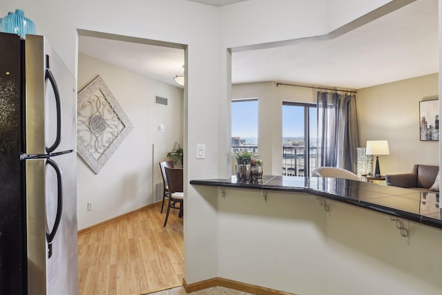 kitchen featuring visible vents, light wood-type flooring, baseboards, freestanding refrigerator, and tile counters
