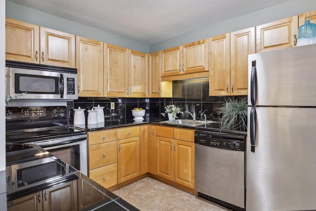 kitchen with light brown cabinets, a textured ceiling, tasteful backsplash, a sink, and appliances with stainless steel finishes