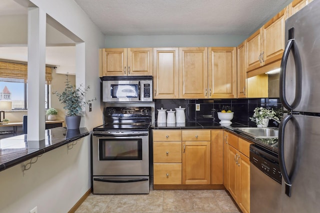 kitchen featuring baseboards, a textured ceiling, a sink, backsplash, and stainless steel appliances