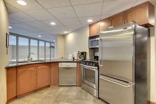 kitchen featuring stone finish flooring, appliances with stainless steel finishes, dark countertops, a sink, and recessed lighting