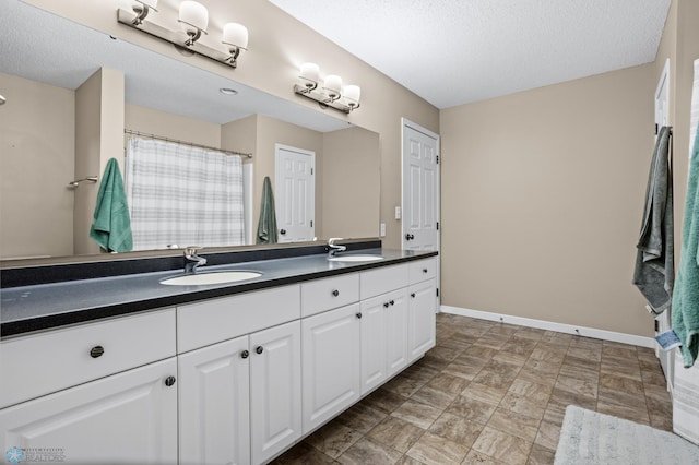 full bathroom featuring baseboards, double vanity, a textured ceiling, and a sink