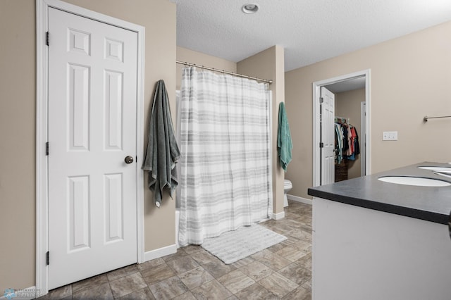 full bath with double vanity, a textured ceiling, a sink, baseboards, and toilet