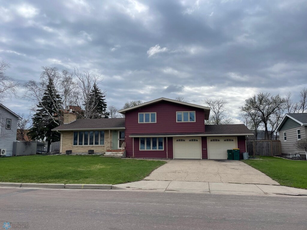 split level home featuring a front lawn, fence, a chimney, and concrete driveway