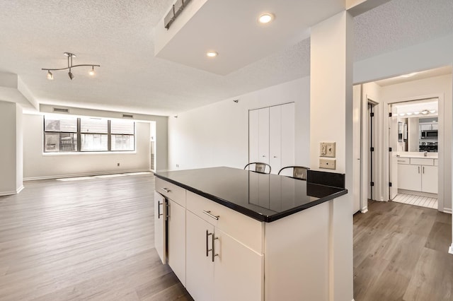 401 1st St Unit 414, Minneapolis, MN 55401 - kitchen featuring light wood-style flooring, dark countertops, a textured ceiling, stainless steel microwave, and open floor plan
