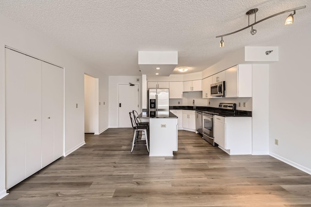 401 1st St Unit 414, Minneapolis, MN 55401 - kitchen featuring stainless steel appliances, a textured ceiling, dark countertops, white cabinets, and a kitchen bar