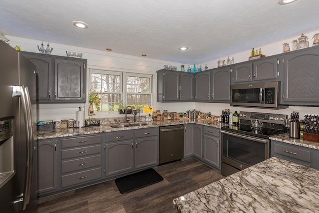 kitchen featuring recessed lighting, dark wood-type flooring, light stone counters, a sink, and appliances with stainless steel finishes