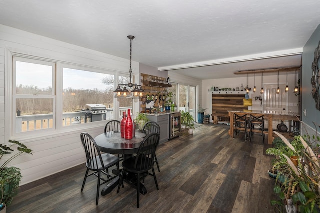 dining space with dark wood finished floors, a bar, an inviting chandelier, and wine cooler