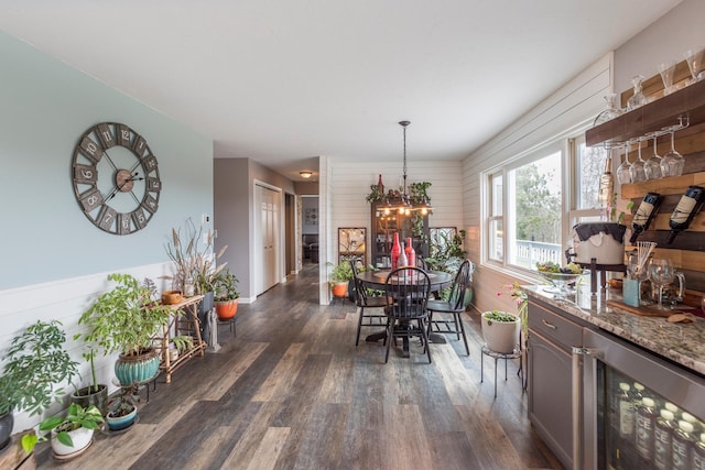 dining room featuring an inviting chandelier, wood walls, dark wood-style flooring, and beverage cooler