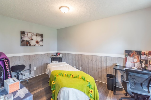 bedroom with a wainscoted wall, a textured ceiling, wood walls, and wood finished floors