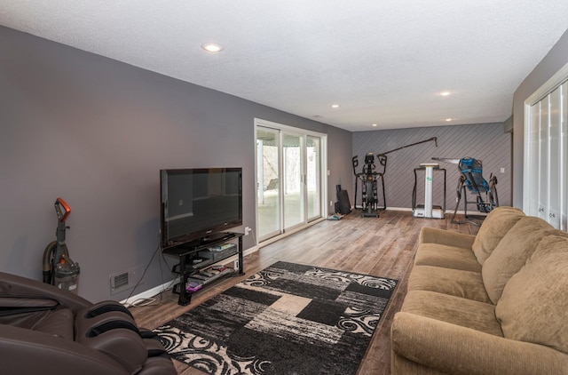 living area with visible vents, wood finished floors, baseboards, an accent wall, and recessed lighting