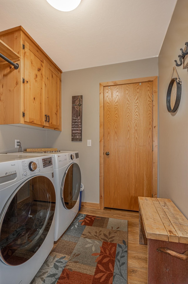 clothes washing area with baseboards, light wood-type flooring, cabinet space, and washer and dryer