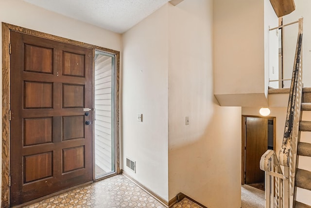 foyer with baseboards, a textured ceiling, light floors, and visible vents