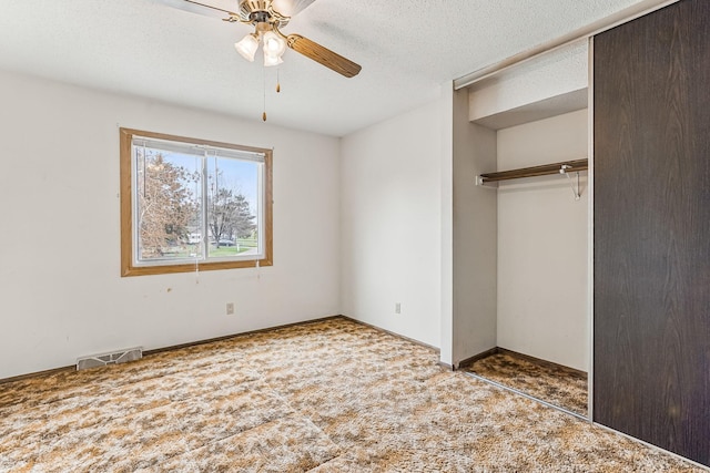 unfurnished bedroom with ceiling fan, a textured ceiling, carpet, visible vents, and a closet
