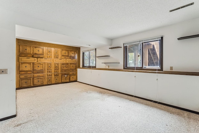 carpeted empty room with a textured ceiling, visible vents, and baseboards