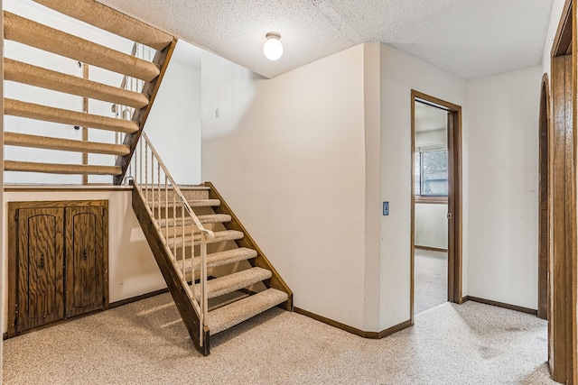 staircase featuring baseboards, carpet, and a textured ceiling