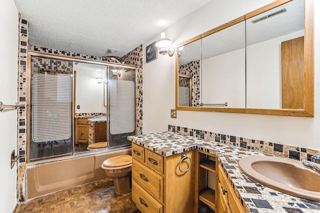 full bathroom with a textured ceiling, visible vents, vanity, toilet, and shower / bath combination with glass door