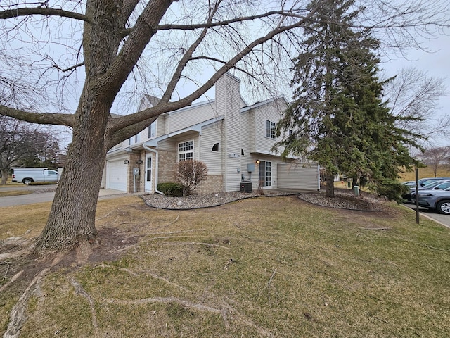 view of side of home with an attached garage, brick siding, a yard, and a chimney