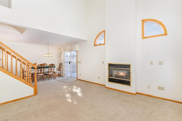 carpeted living room with baseboards, a multi sided fireplace, a high ceiling, and a chandelier