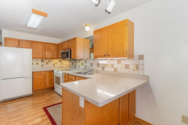 kitchen with a peninsula, white appliances, light countertops, a sink, and light wood-style flooring