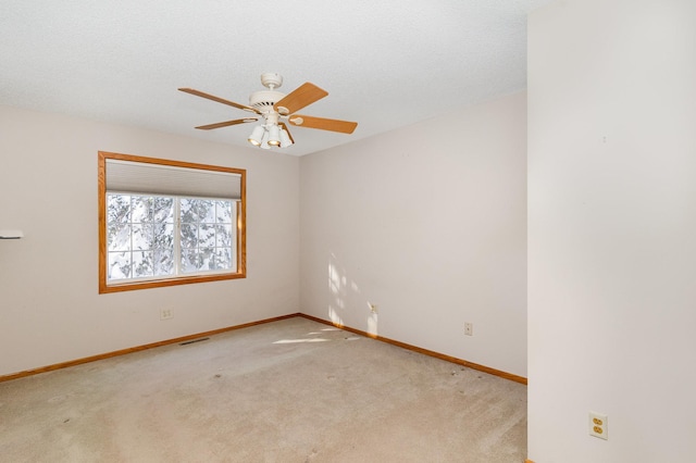 carpeted spare room with baseboards, a ceiling fan, and visible vents