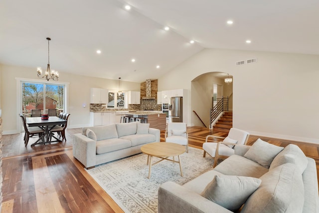 living room featuring stairs, wood finished floors, lofted ceiling, arched walkways, and a notable chandelier