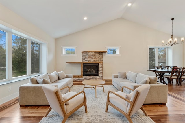 living area with plenty of natural light, vaulted ceiling, a stone fireplace, and an inviting chandelier