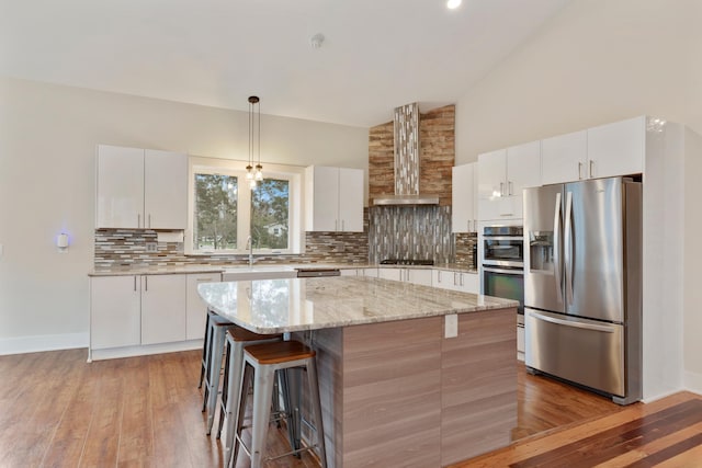 kitchen with backsplash, stainless steel appliances, a kitchen island, and wall chimney range hood