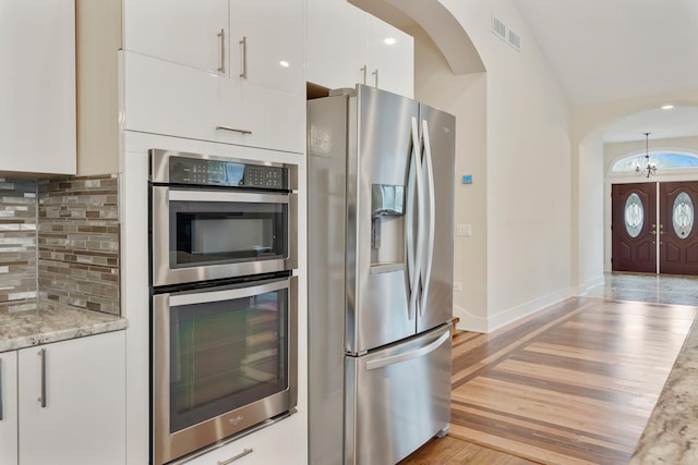 kitchen with visible vents, decorative backsplash, white cabinetry, arched walkways, and appliances with stainless steel finishes