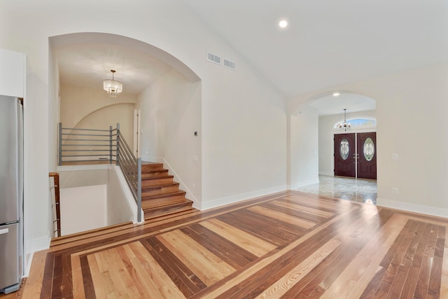 foyer entrance with an inviting chandelier, wood-type flooring, arched walkways, lofted ceiling, and stairway