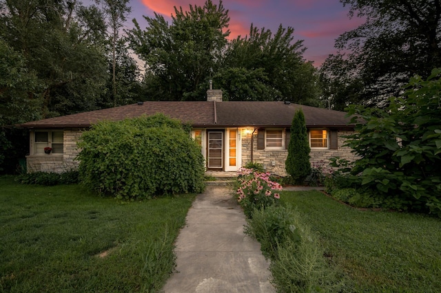 single story home with a chimney, a yard, and stone siding