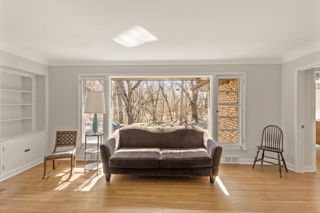 living area with visible vents, built in shelves, a wealth of natural light, and light wood-style floors