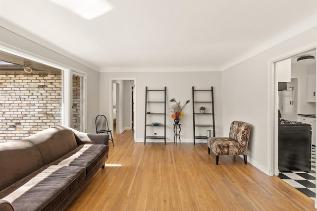 living area featuring light wood-type flooring, baseboards, and brick wall