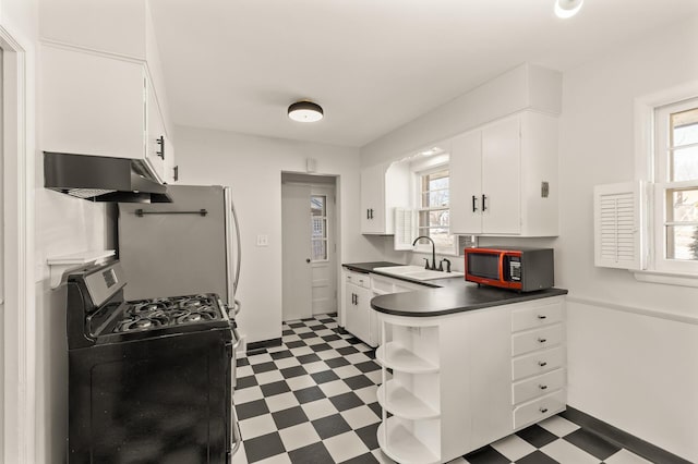 kitchen with dark countertops, stainless steel gas stove, a sink, dark floors, and under cabinet range hood