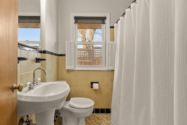 bathroom featuring a sink, a wealth of natural light, toilet, and tile walls