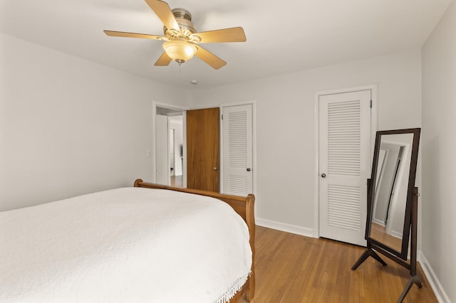 bedroom featuring two closets, a ceiling fan, baseboards, and wood finished floors