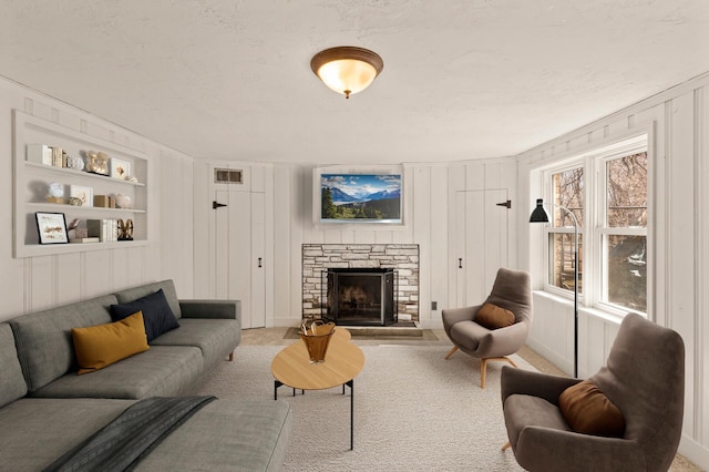 carpeted living room featuring a stone fireplace, built in features, a decorative wall, and visible vents