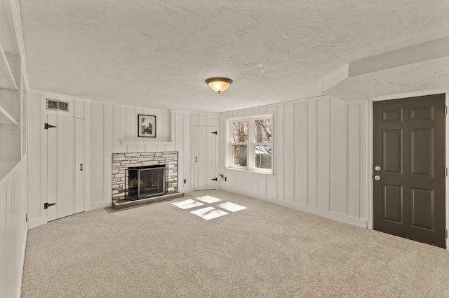 unfurnished living room featuring visible vents, carpet flooring, a decorative wall, and a stone fireplace