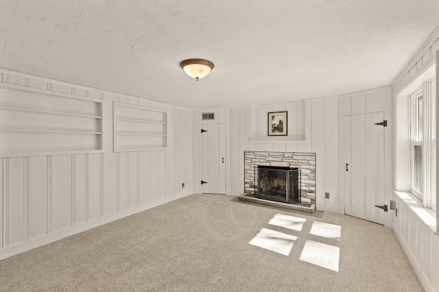 unfurnished living room with built in shelves, a fireplace, a decorative wall, and a textured ceiling